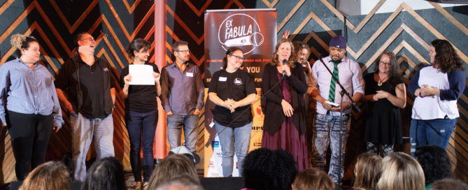 9 Adults standing in a line on stage reviewing their stories