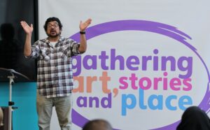 José in front of Gathering Art Stories and Place banner