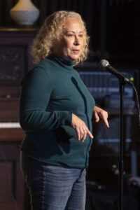 Woman with curly blonde hair stands at microphone to tell story