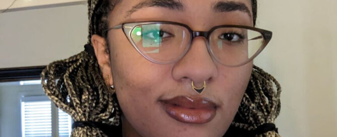 A Black, non-binary person with ombre blonde braids and glasses.