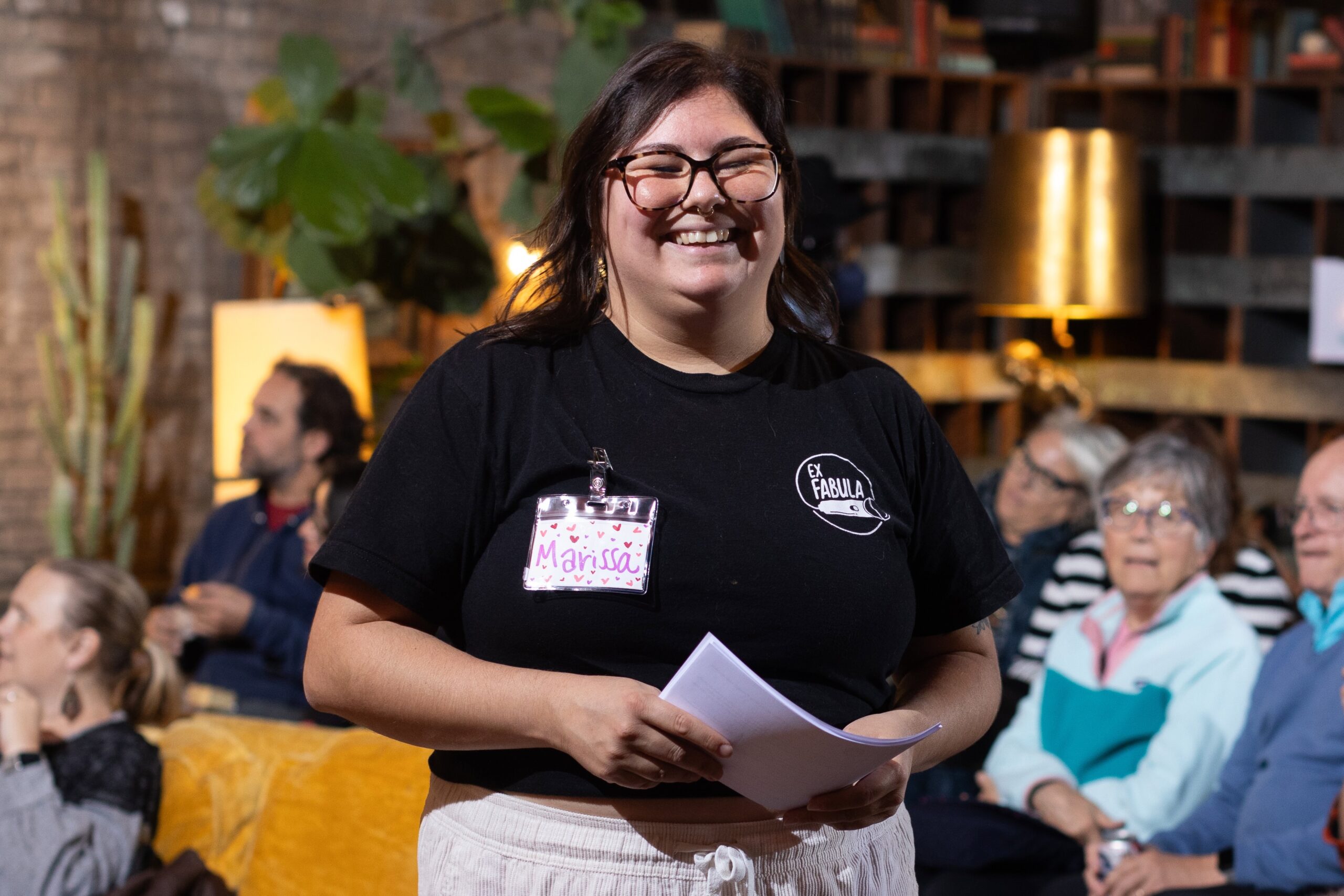 Picture of Ex Fabula staffer Marissa holding a stack of papers and smiling at an event