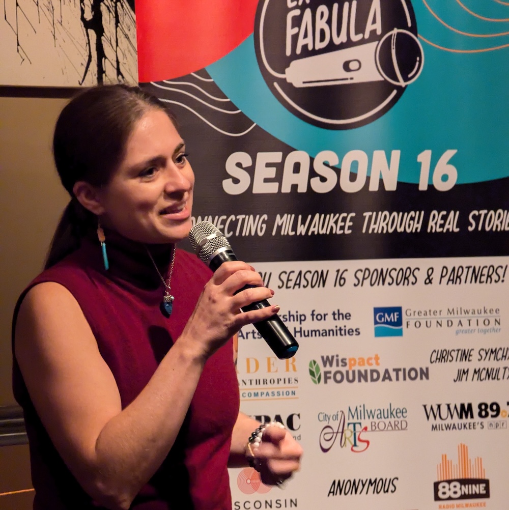 Person holding a microphone, standing in front of a large vertical vinyl banner with corporate logos on it