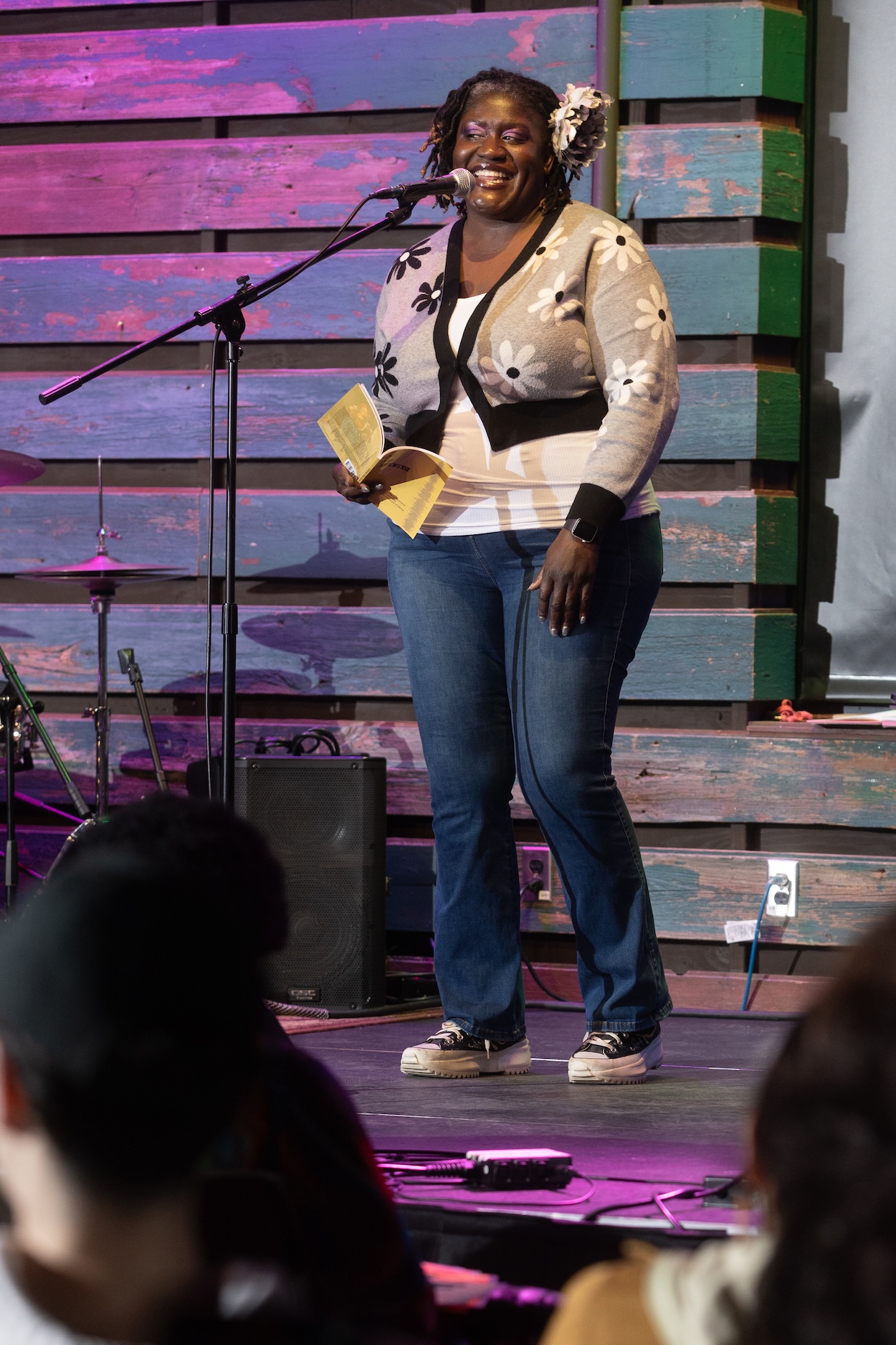 Person standing on a stage, speaking into a microphone while holding a book in their right hand.