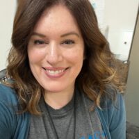 Kristina edited Smiling woman with light skin and auburn wavy hair. She is wearing a gray tshirt and a blue zip up sweatshirt.