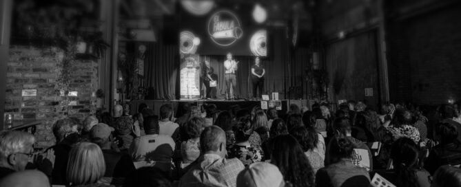 black and white image of an audience looking at the stage. The top of the photo has been blurred to focus more on the audience.
